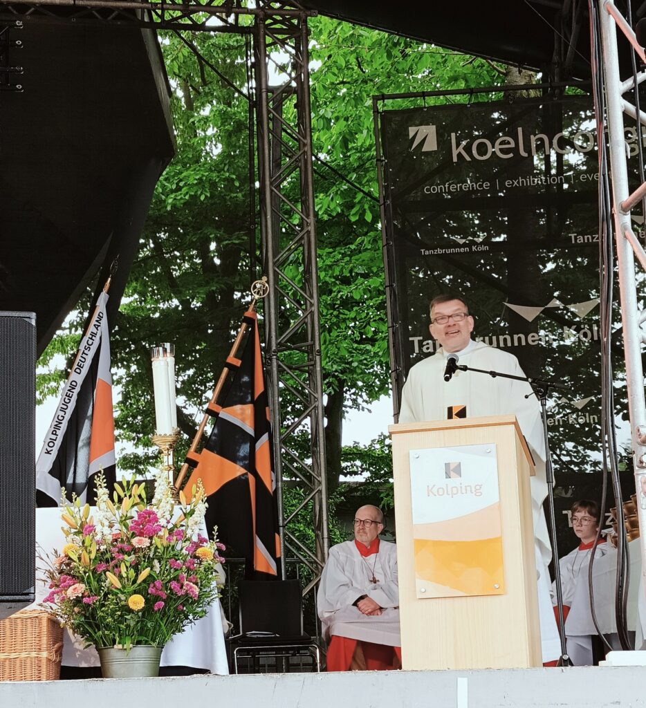 Ujęcie księdza przemawiającego w szatach z logiem KOLPING