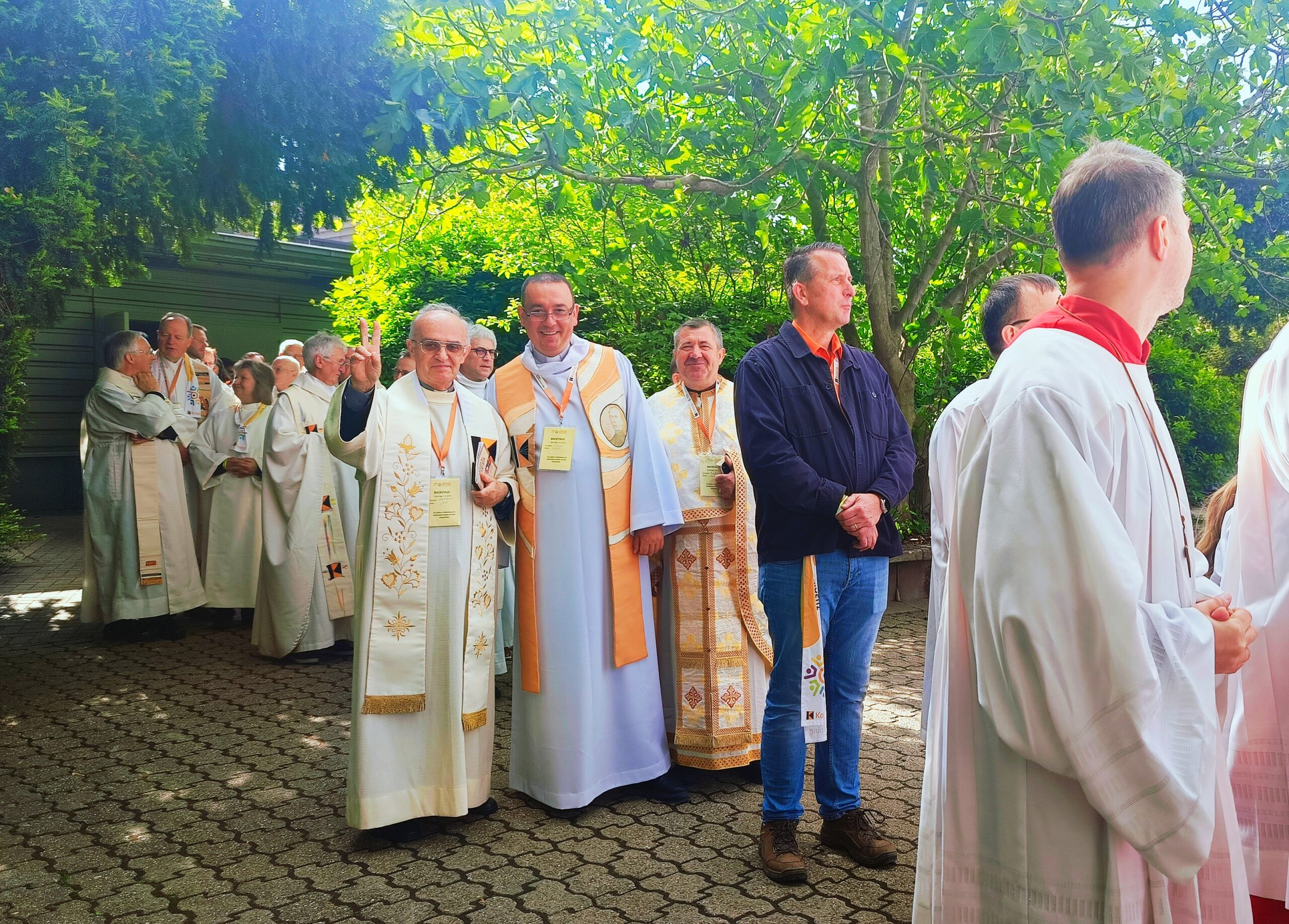 Ujęcie trzech księży pozujących do zdjęcia w szatach z akcentami pomarańczowymi. Uśmiechają się do zdjęcia