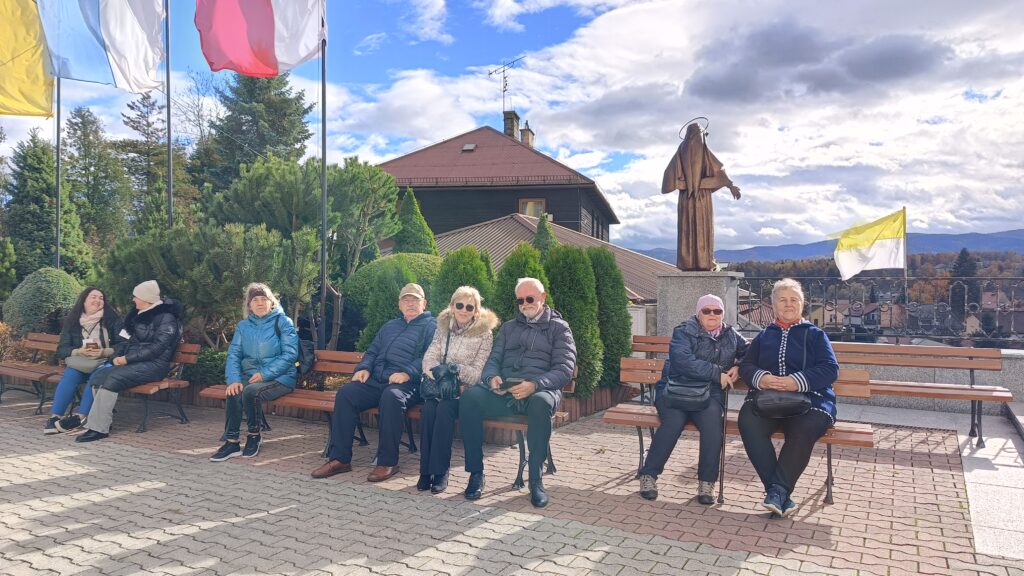 zdjęcie przedstawia grupę osob siedzących przed kościołem